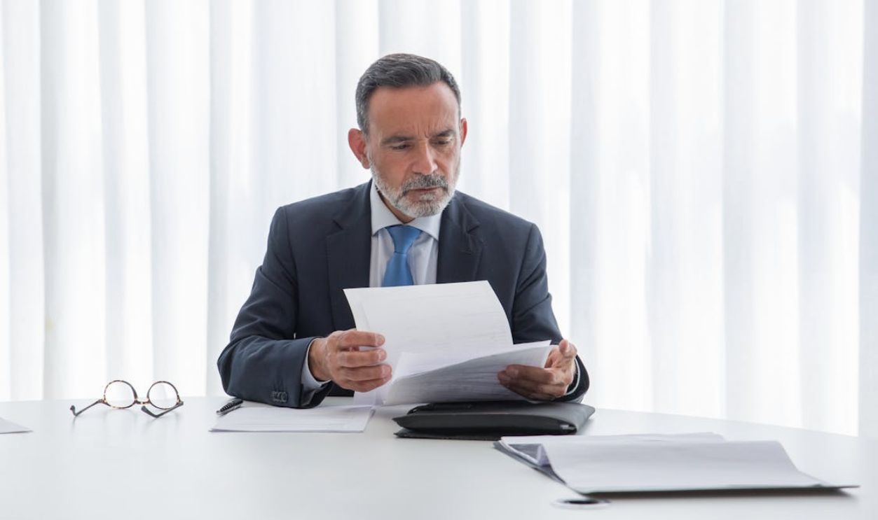 An Elderly Man in Suit Reading the Document he is Holding