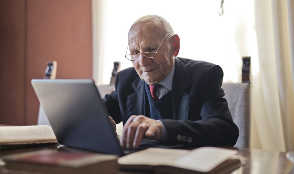 Serious senior man using laptop while sitting at table with books