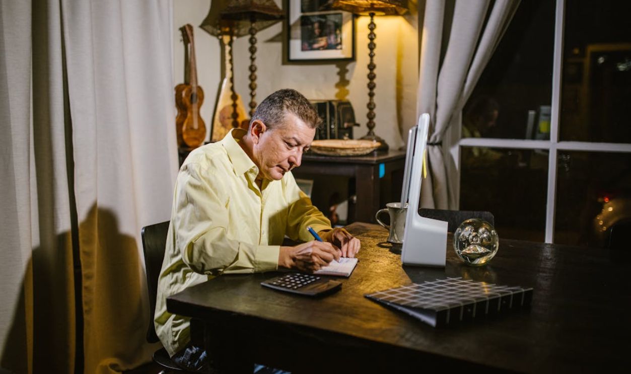 An Elderly Man Sitting while Writing on Notebook