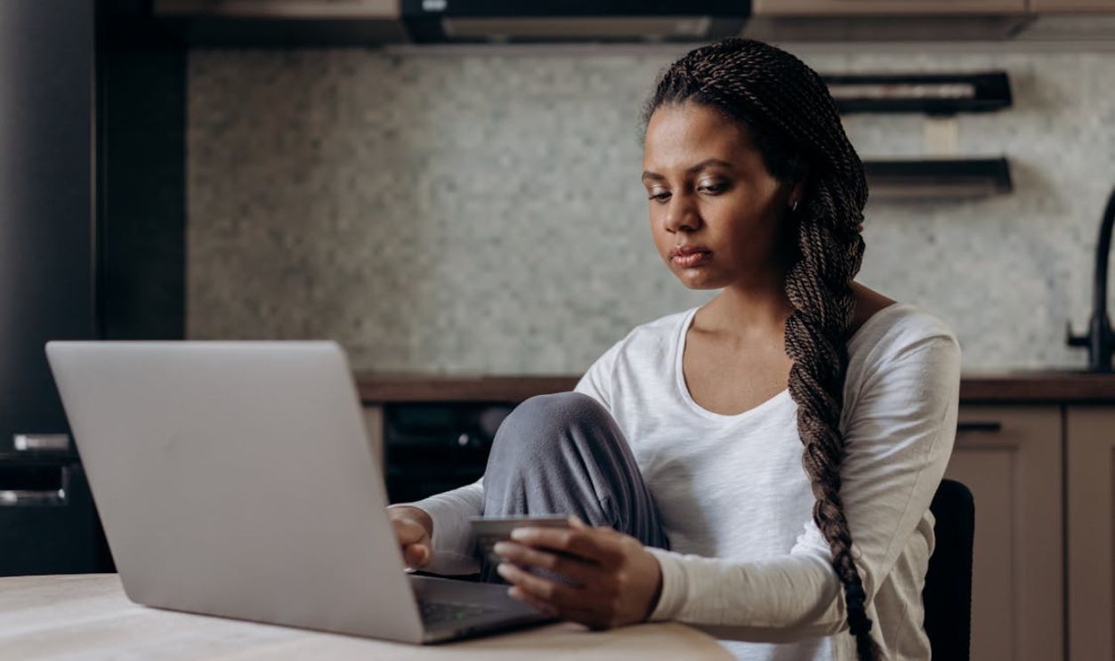Woman in White Long Sleeve Shirt Sitting by the Table while Using Laptop