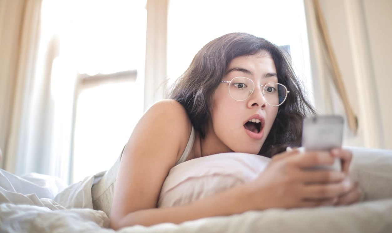 Woman Lying on Bed Holding Smartphone