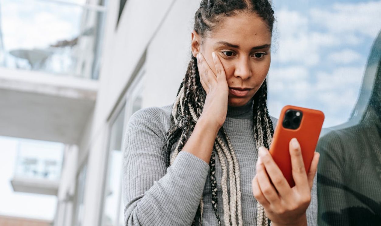 Crop concerned black woman using smartphone on street