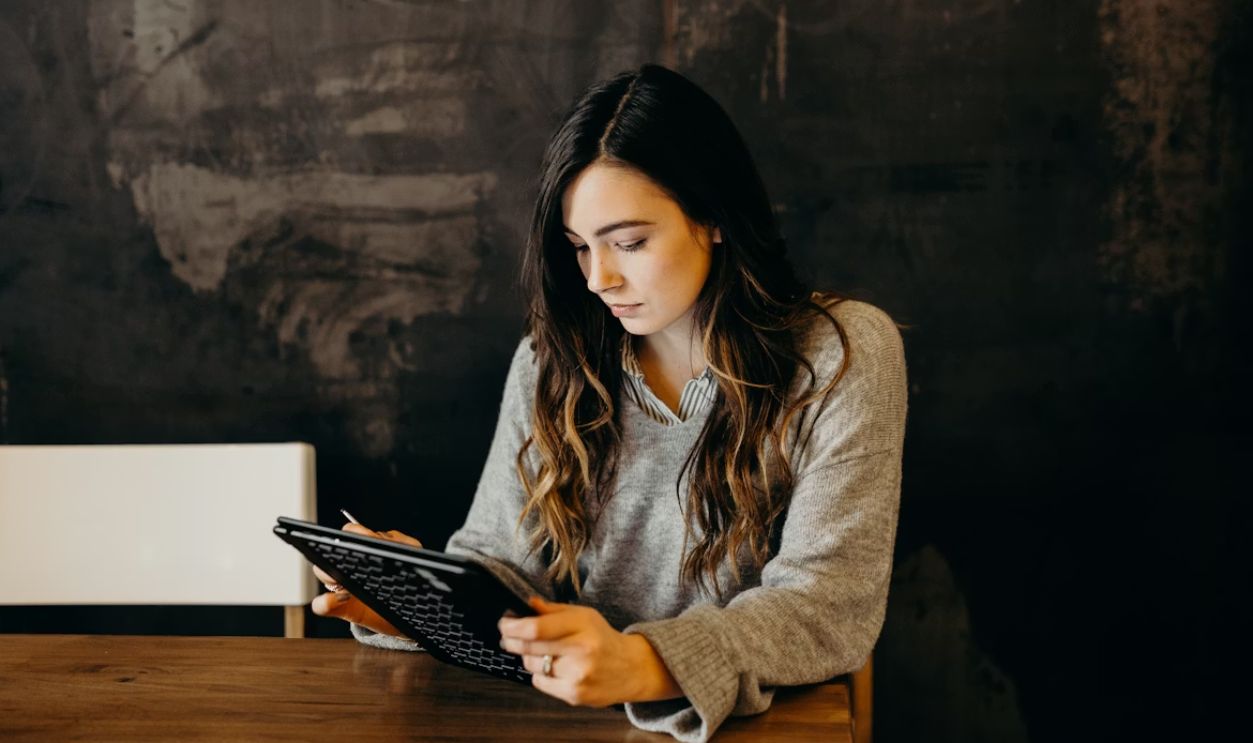woman wearing white dress shirt using holding black leather case on brown wooden table
