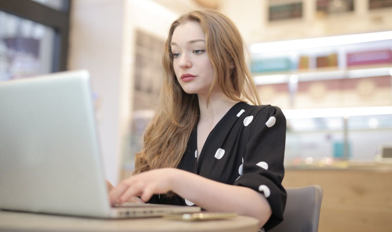 Woman in Black and White Polka Dots Dress Using Silver Laptop