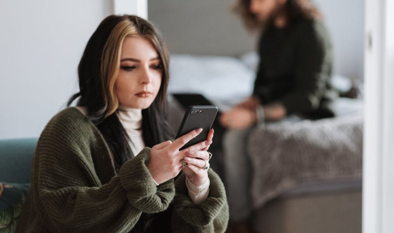 Thoughtful young woman messaging on smartphone near boyfriend typing on netbook