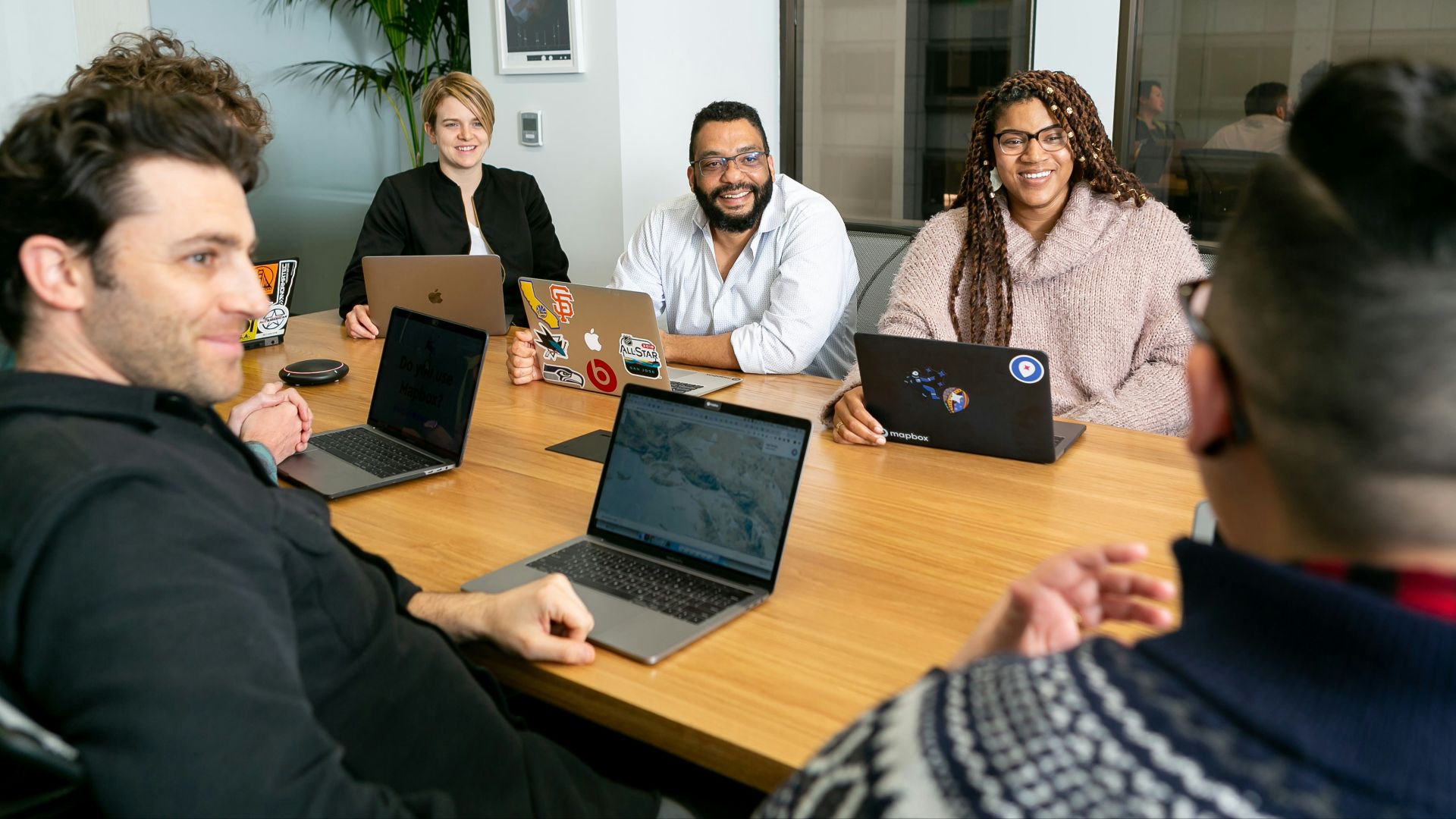 four people all on laptops, two men and two women, listen to person talking in a board meeting