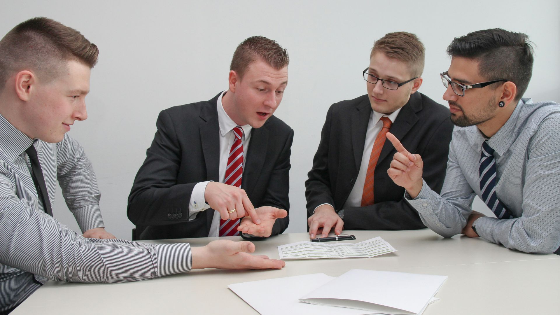 four men sitting at desk talking