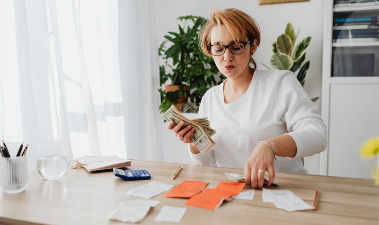 Woman in White Long Sleeves Sitting on the Table Counting Money