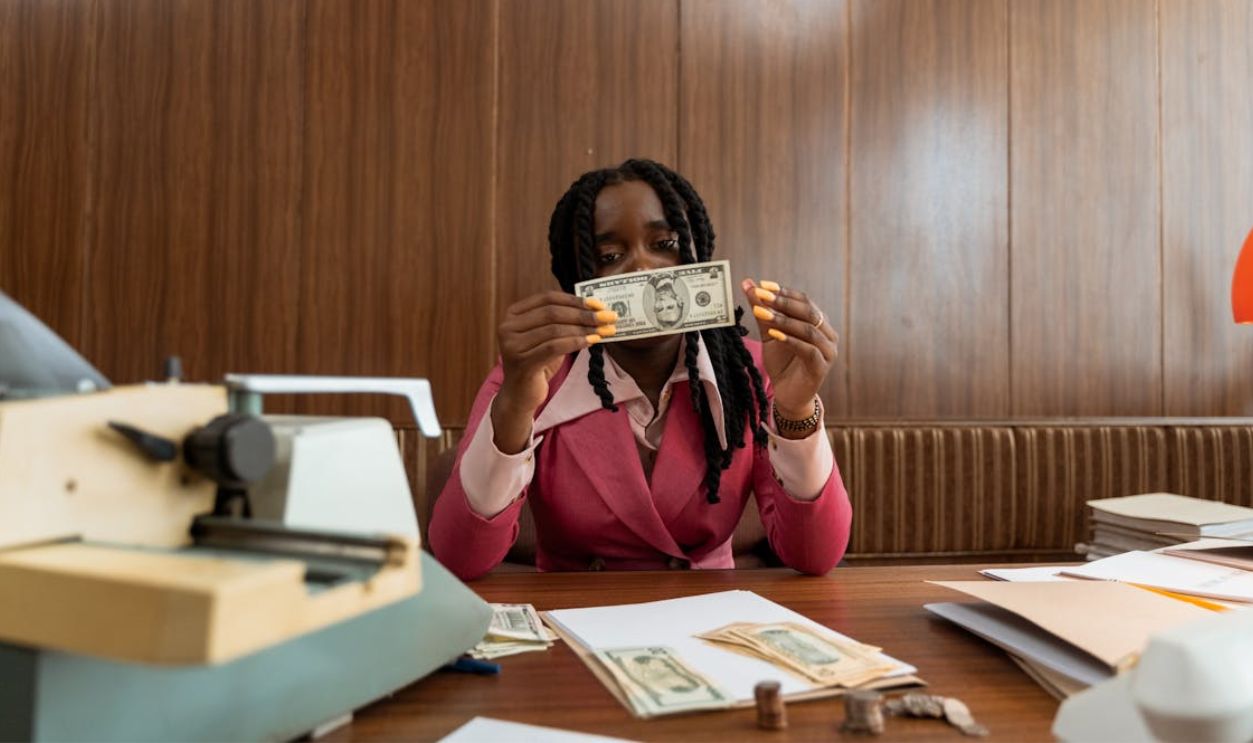 A Woman in Pink Blazer Holding Paper Money Against Face