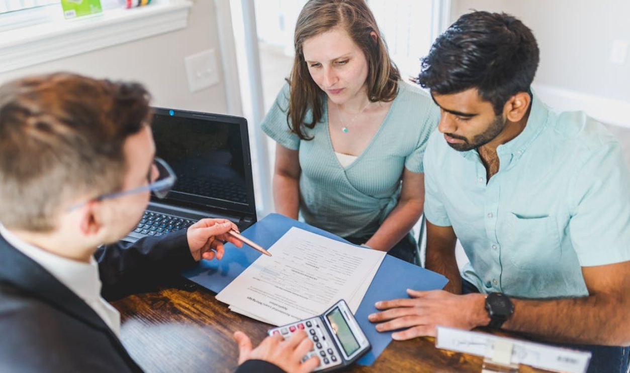 Real Estate Agent in Black Coat Discussing an Ownership Agreement to a Couple Inside the Office