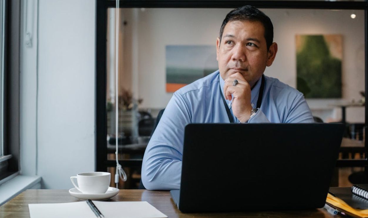 Thoughtful ethnic businessman using laptop while working in office
