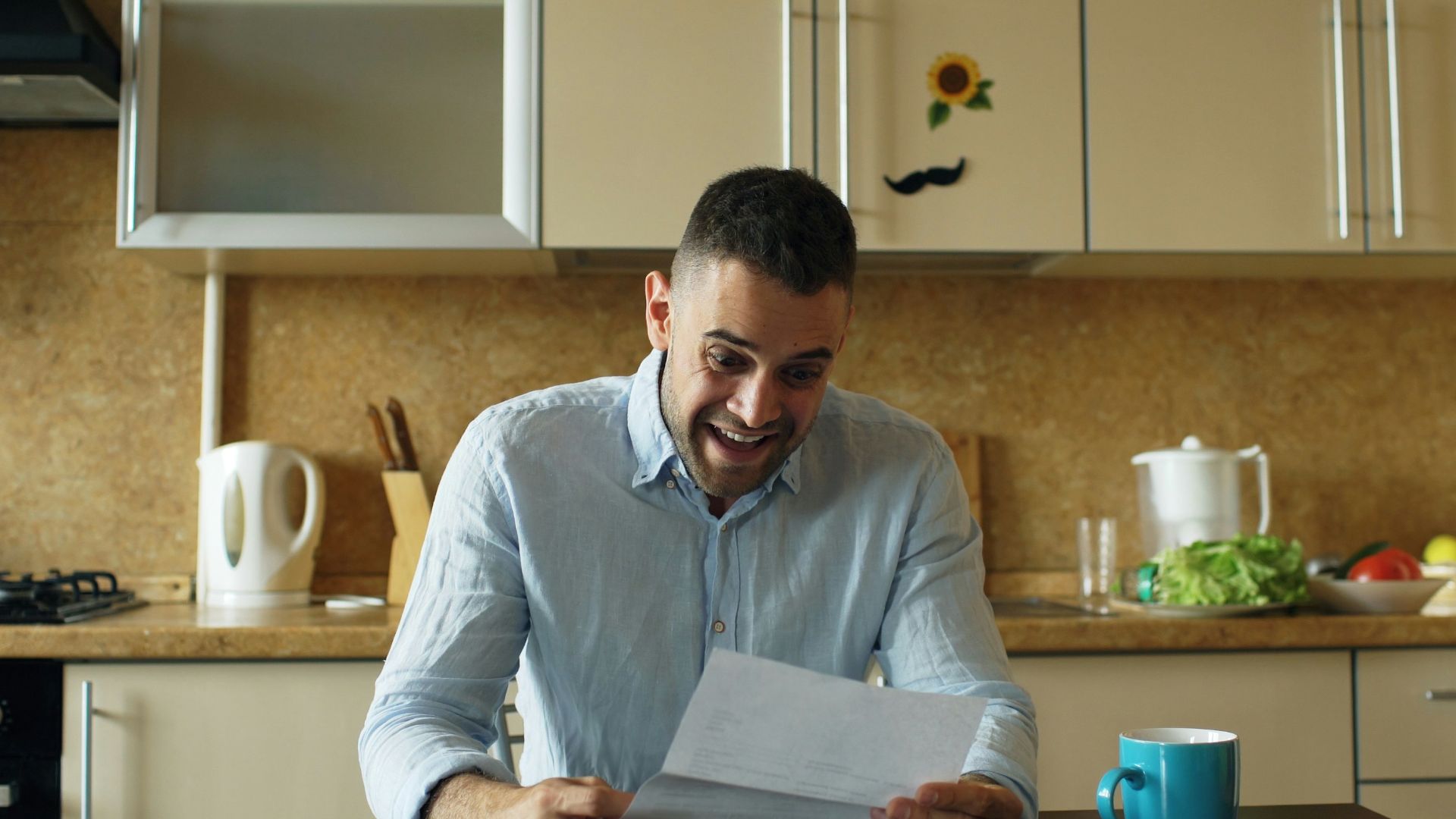 Man reading a letter at a kitchen table.