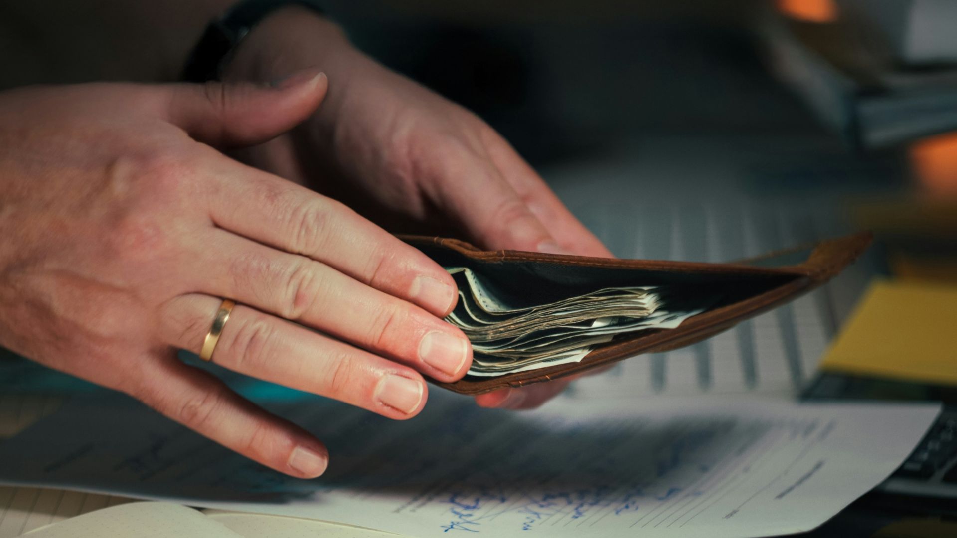 Hands holding cash in a wallet over papers.