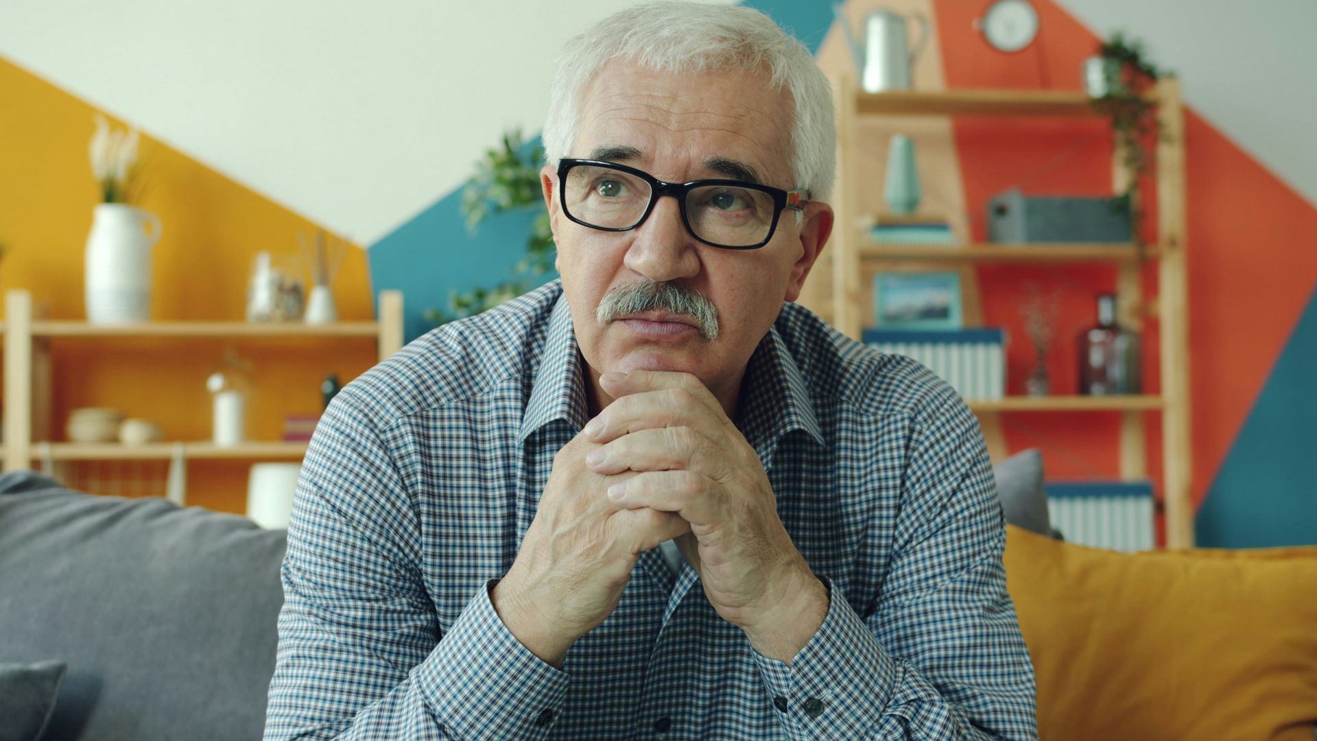Elderly man with glasses resting chin on hands.