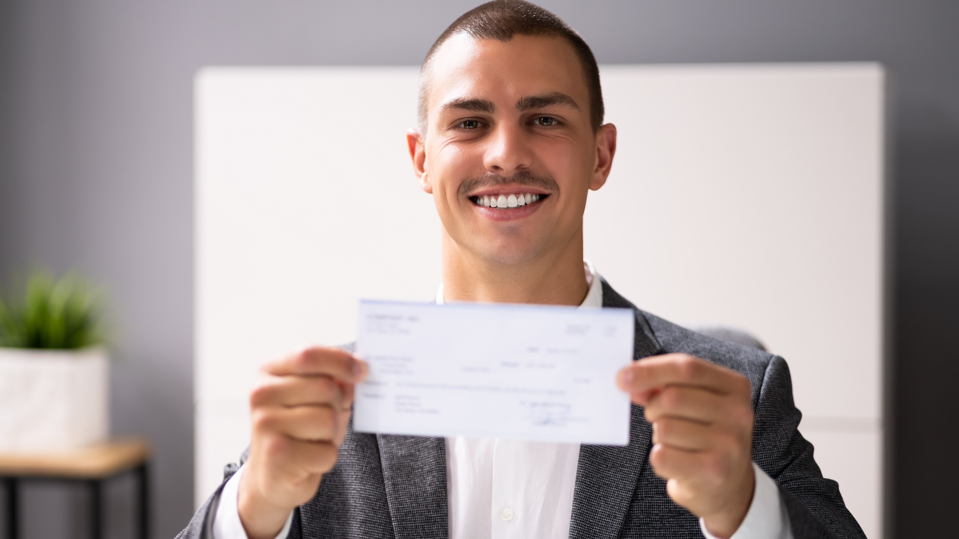 Man is holding a pay check in his hands and smiling at camera.