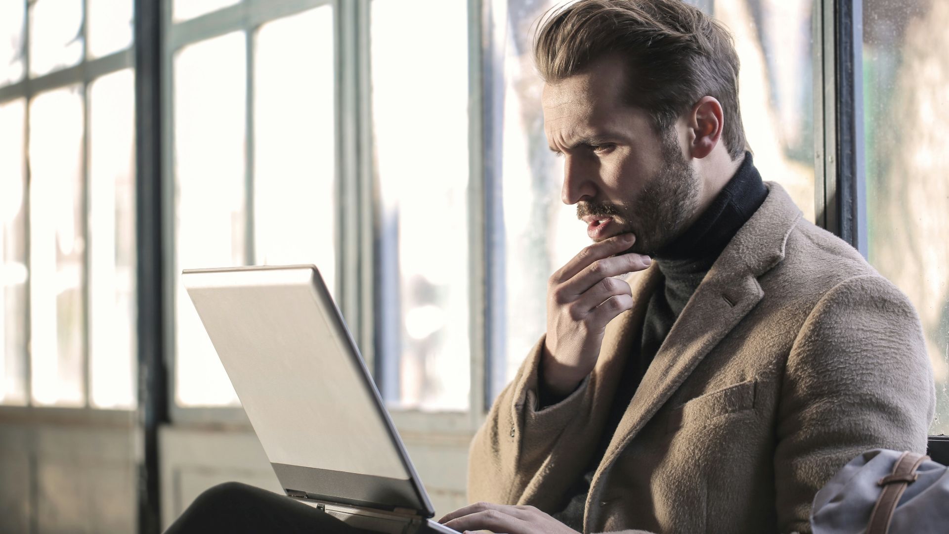 man holding his chin facing laptop computer