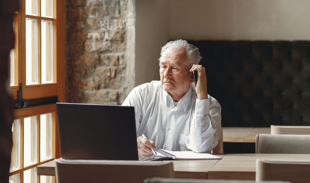 Pensive stylish elderly man speaking on smartphone in creative office