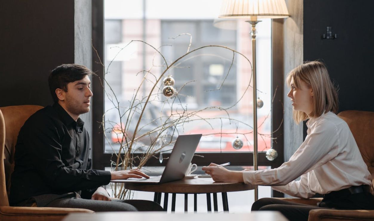 A Woman Sitting at a Table across a Man Using a Laptop