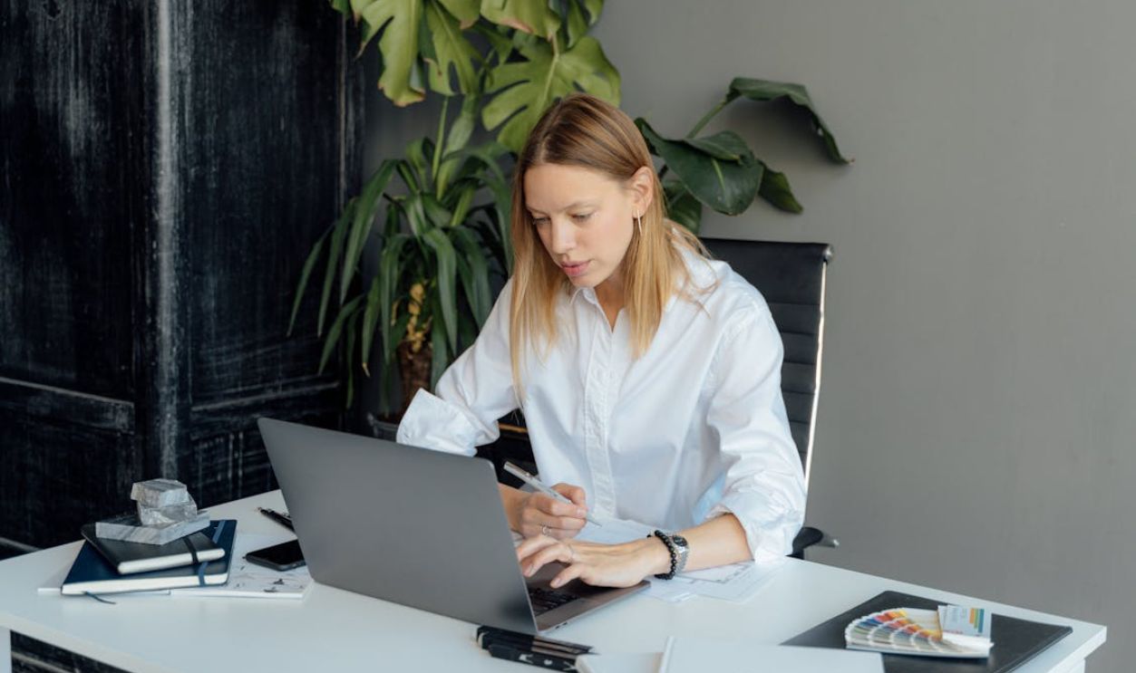 A Woman in White Long Sleeves Typing on Her Laptop