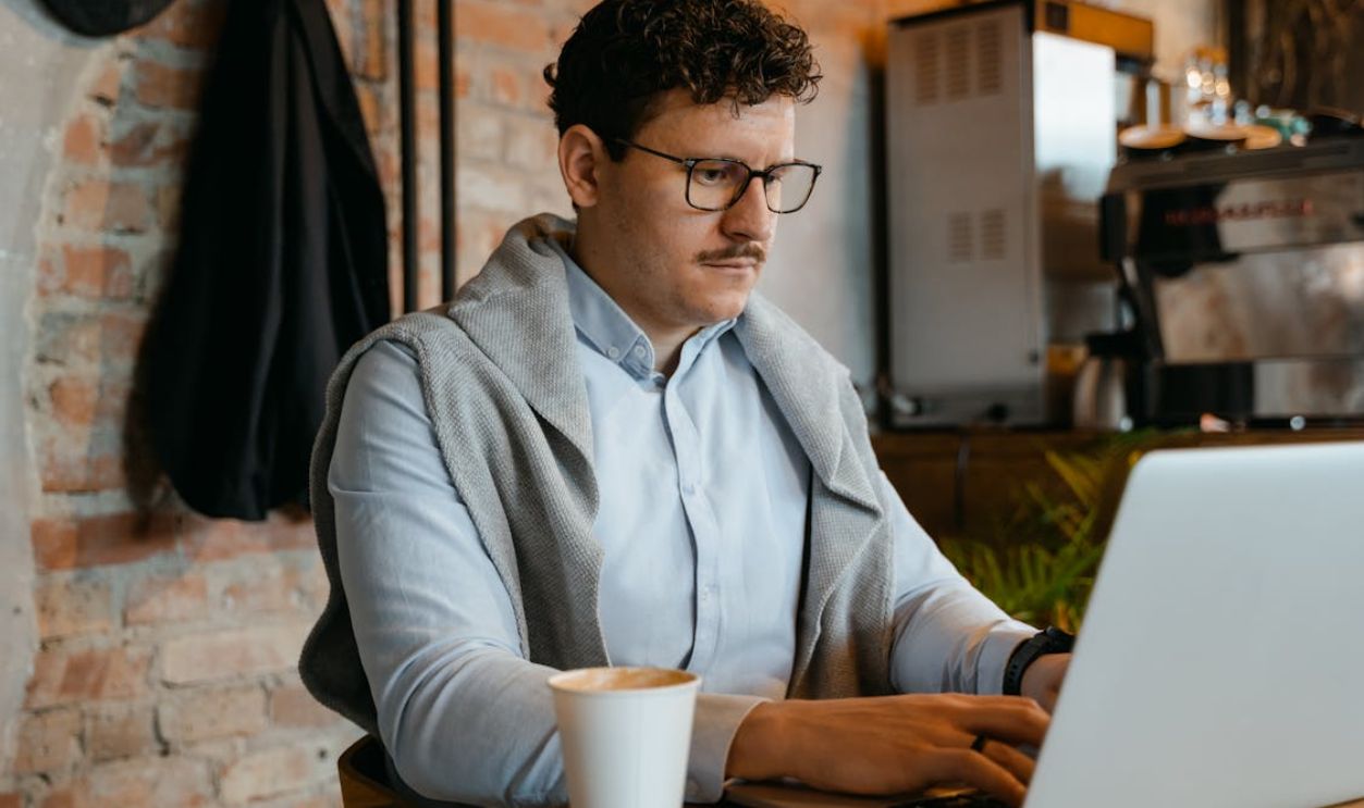 A Coffee Cup beside a Man Typing on Laptop