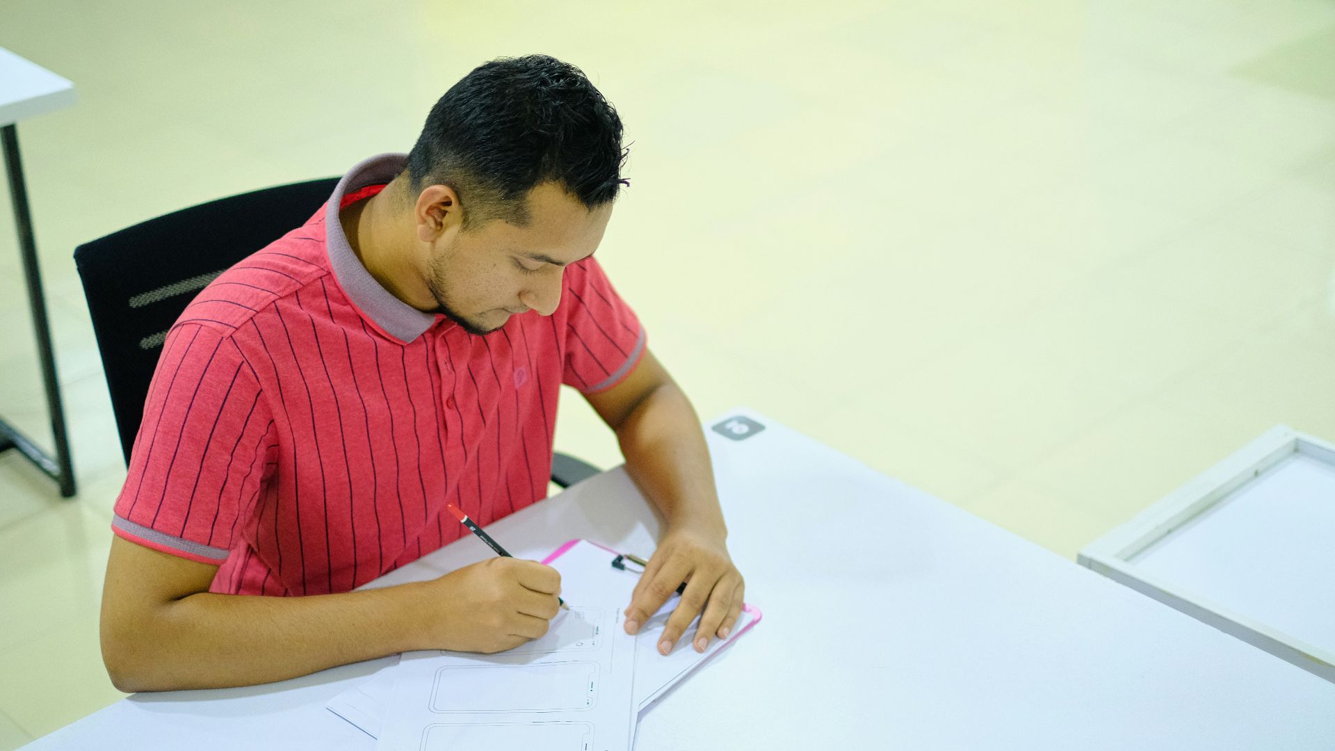 man in red and white striped crew neck t-shirt writing on white paper