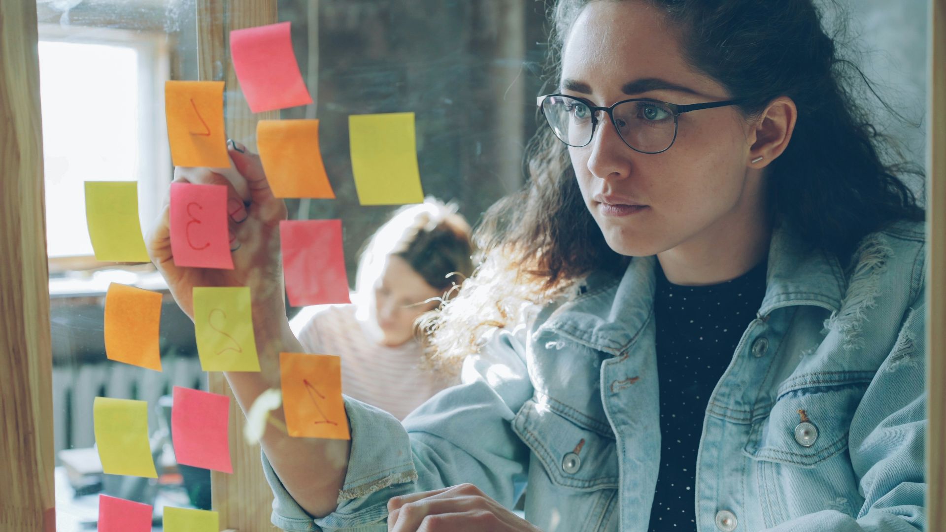 Woman brainstorming with sticky notes on glass.