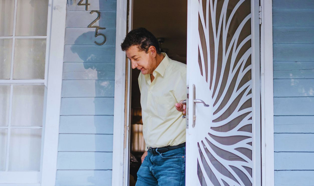 Man in White Dress Shirt and Blue Denim Jeans Standing Beside White Wooden Door