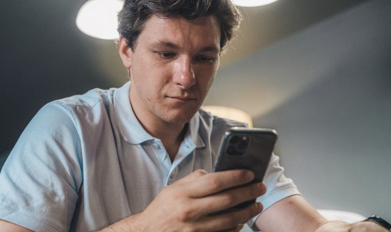 A Man in Blue Button Up Shirt Holding a Black Smartphone