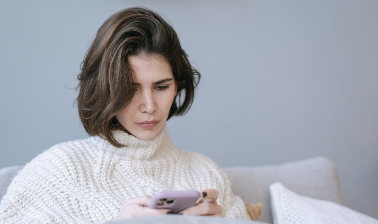 A Woman in White Knitted Sweater Using a Cellphone