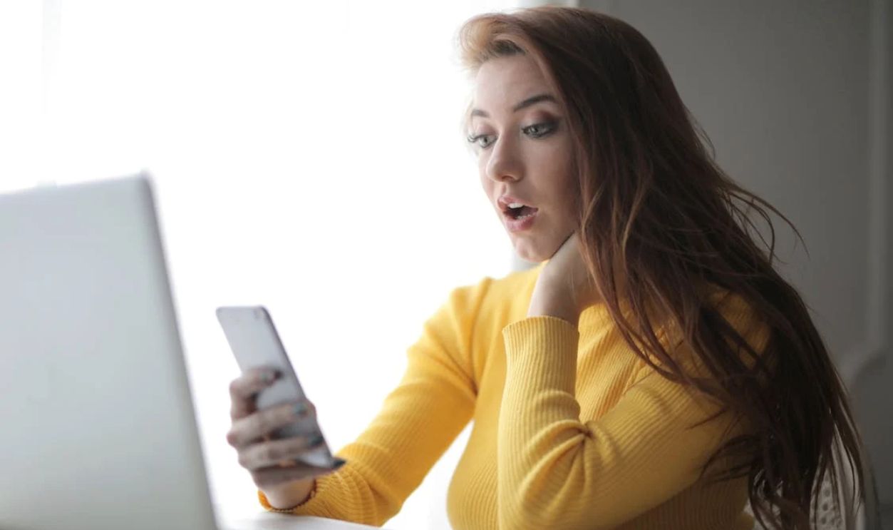 Woman in Yellow Turtleneck Sweater Holding Phone Sitting Beside Laptop