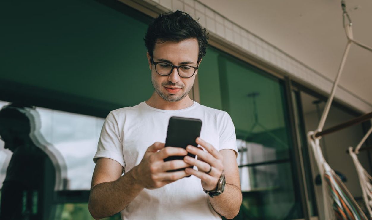A Young Man Using a Smartphone Standing on a Balcony