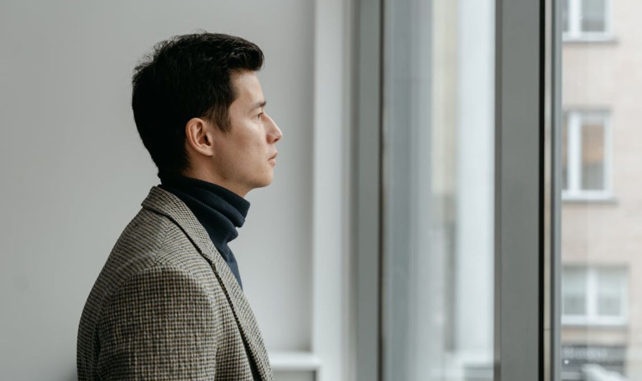 Man in Gray Checkered Suit Looking Outside the Window