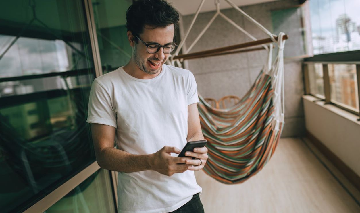 A Young Man Using a Smartphone Standing on a Balcony