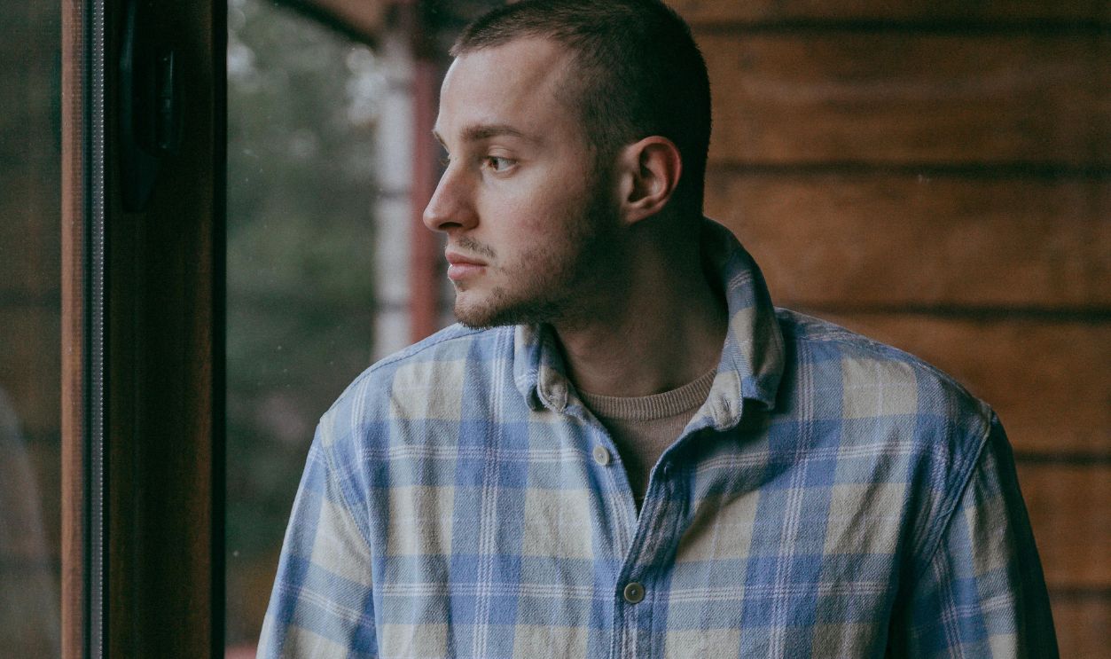 Man in a Checkered Shirt Standing near a Window