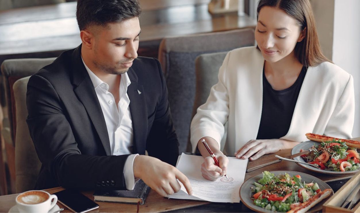 Content ethnic businesswoman signing contract while sitting with partner
