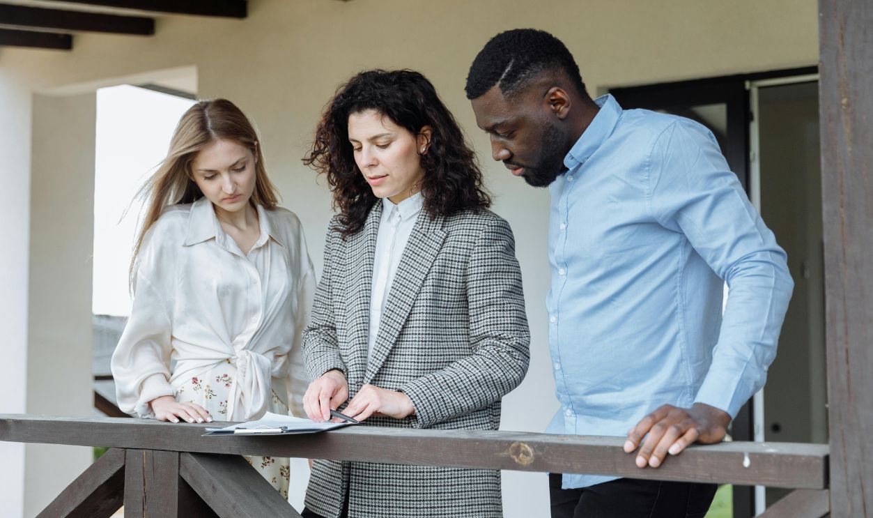 People Standing Near Wooden Railing while Looking at the Document on the Clipboard