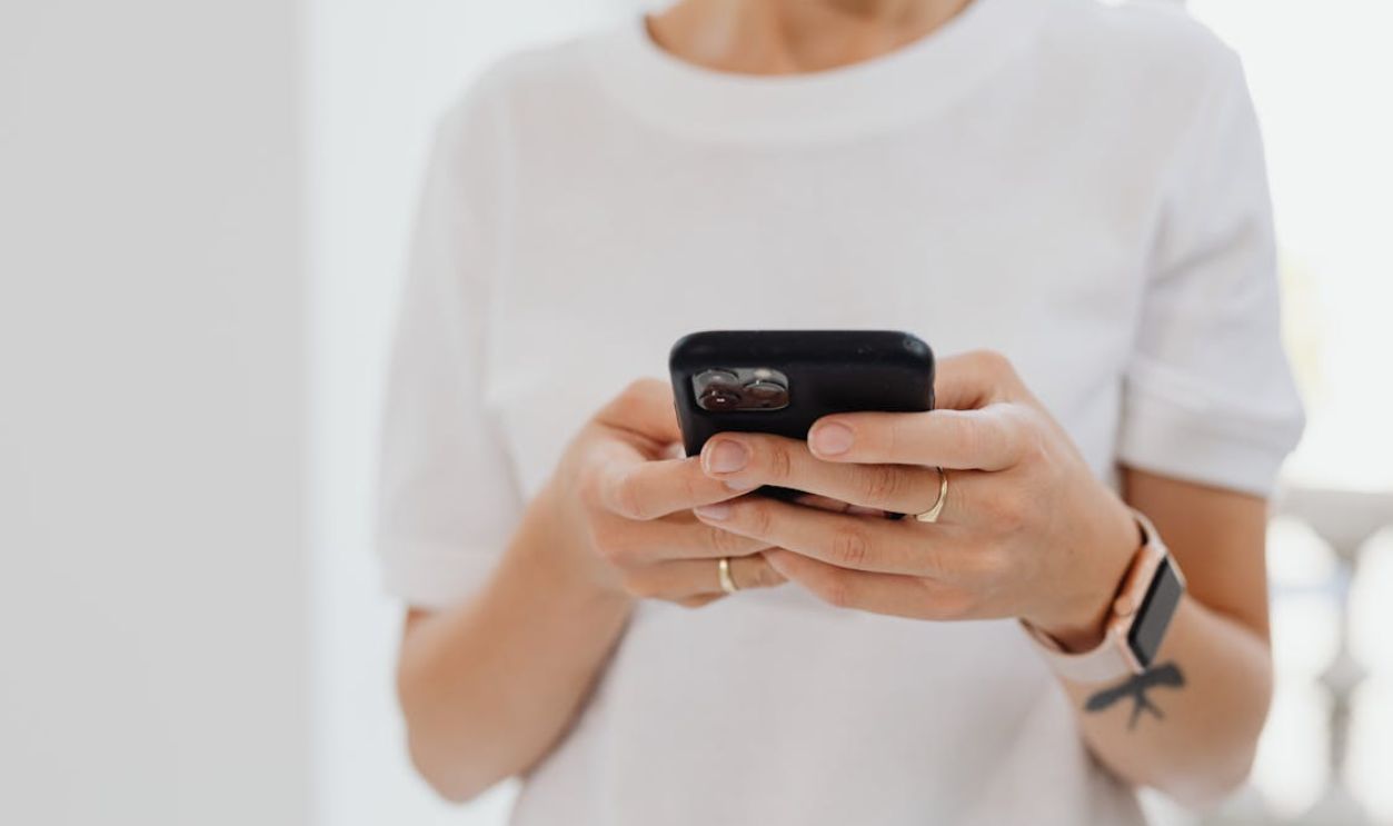 A Woman in White Crew Neck Shirt Holding a Black Smartphone