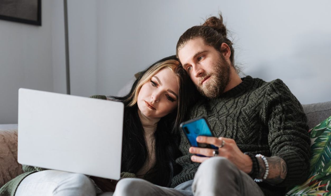 Couple with laptop and smartphone on sofa at home
