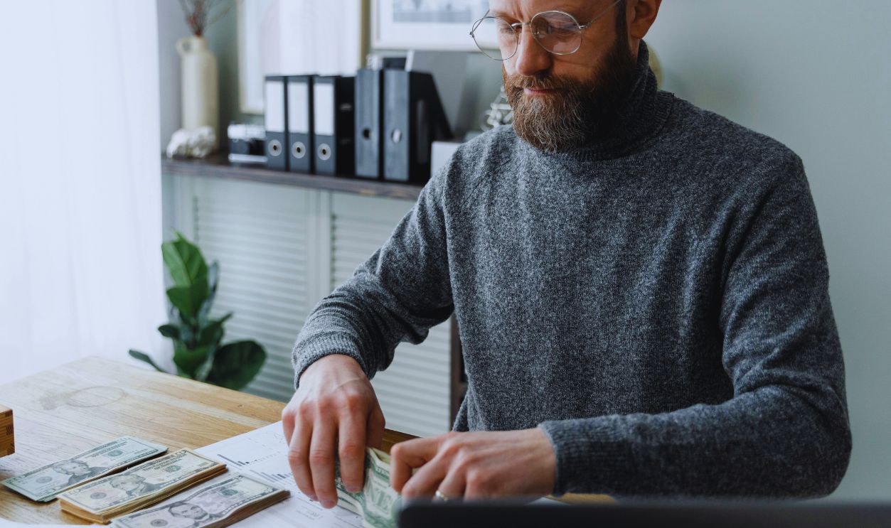 Man in Gray Sweater Wearing Eyeglasses Holding Paper Money