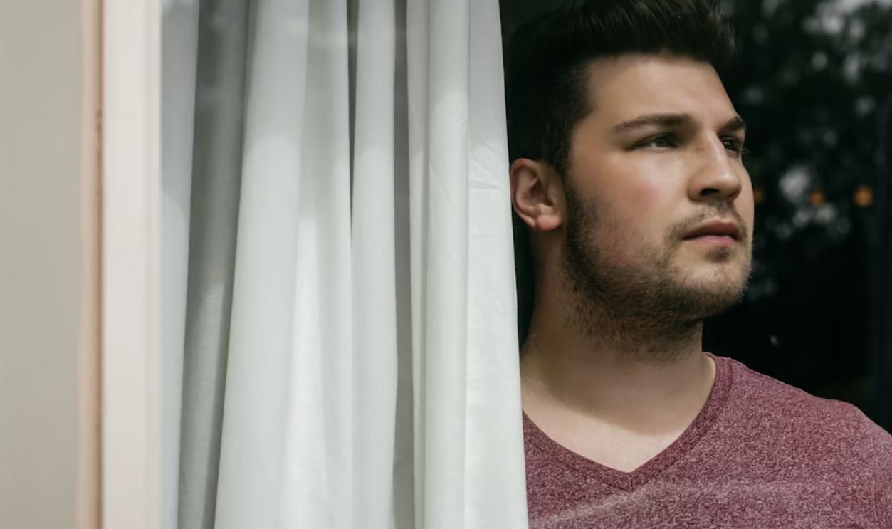 man in red crew neck shirt standing beside white curtain