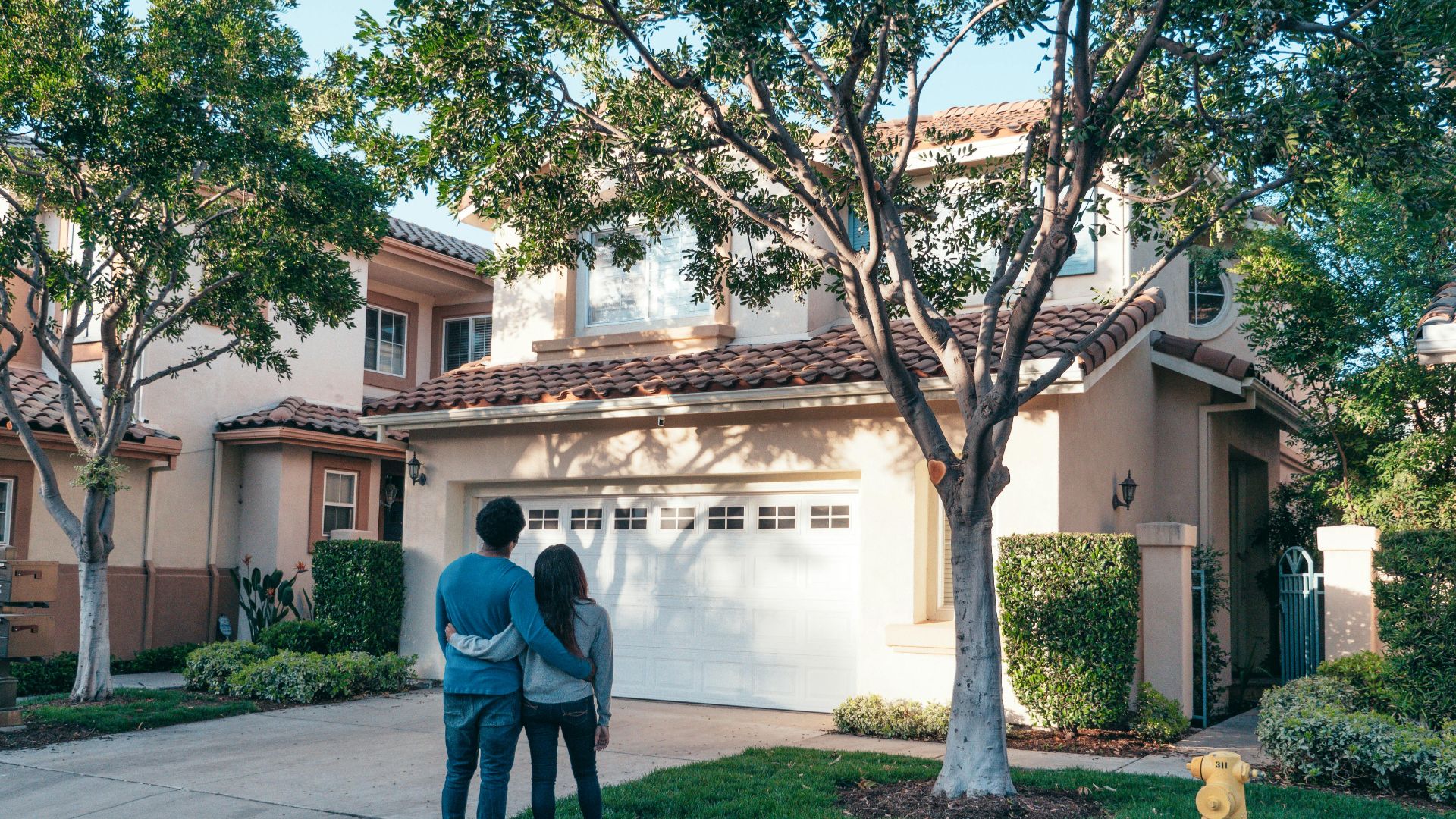 Couple hugging outside their newly purchased suburban home, showcasing togetherness and new beginnings.