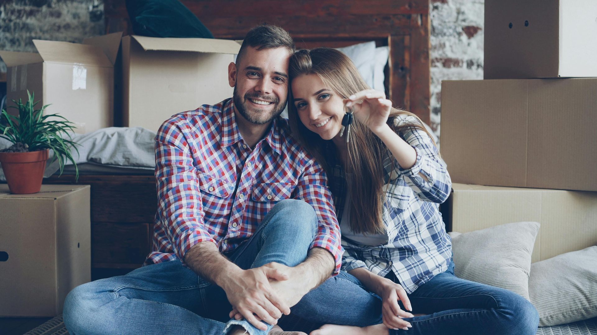Smiling couple holding keys amidst moving boxes at their new home.
