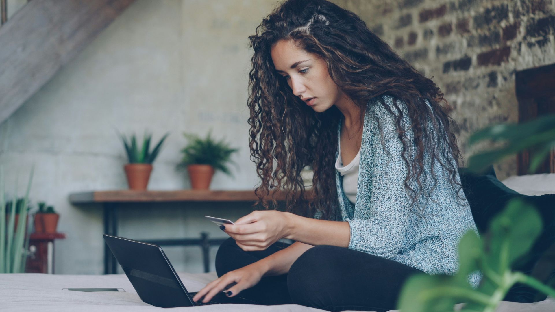 Woman using laptop and credit card on bed.