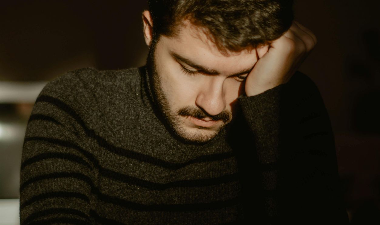 Tired ethnic man leaning on hand at home