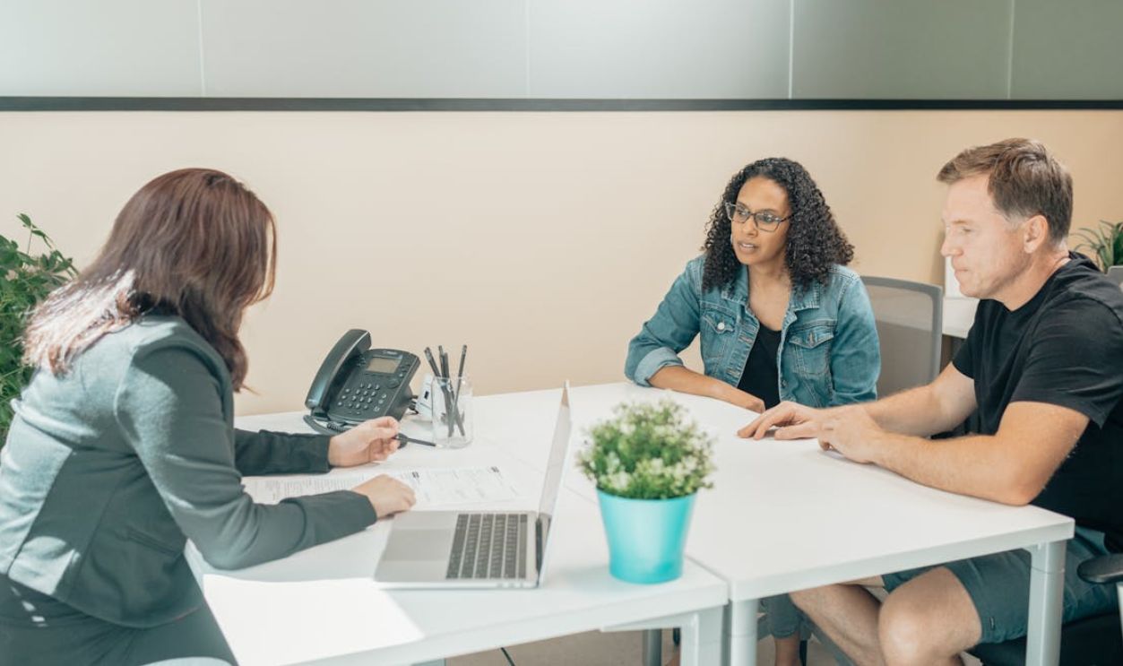 Unrecognizable worker talking to multiethnic clients at desk with laptop