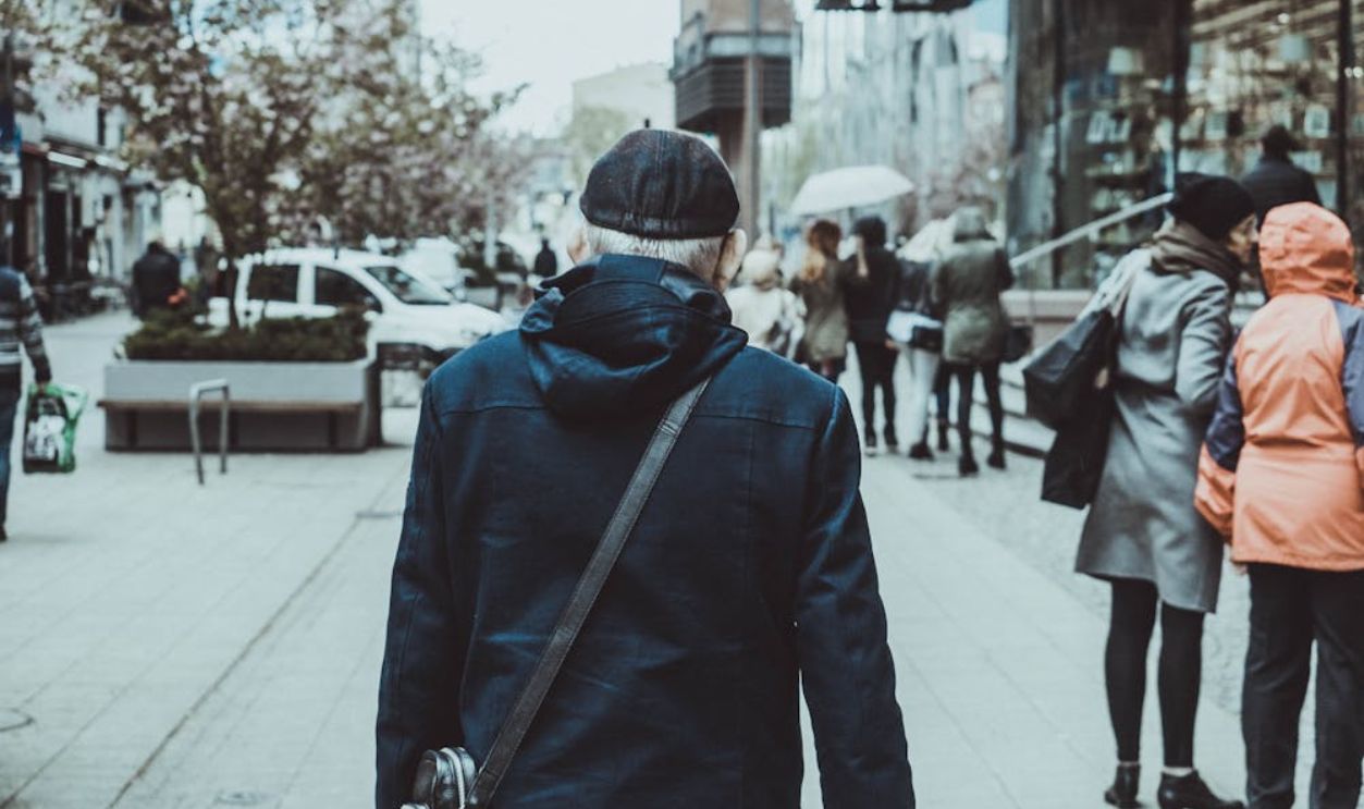 Anonymous elderly man walking on city street on cloudy day