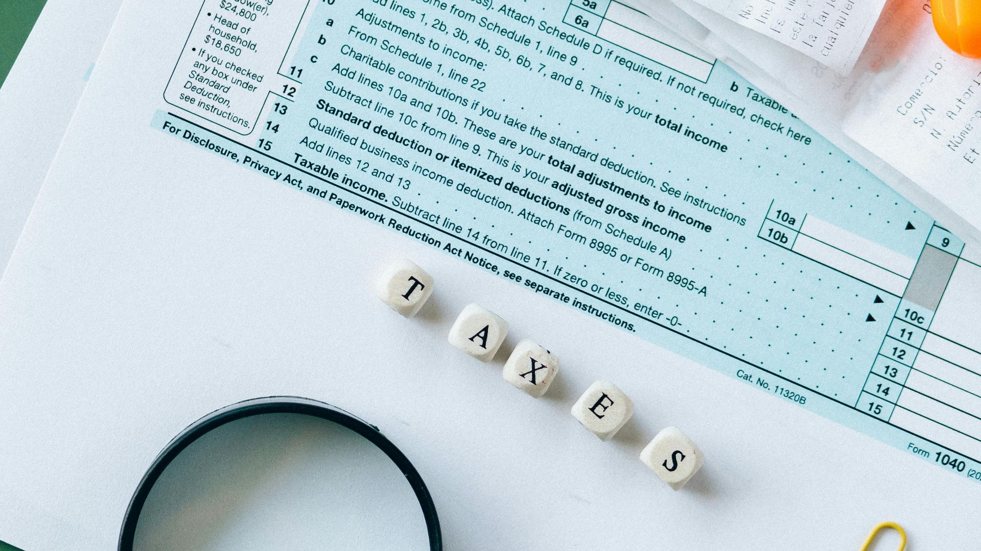 Top view of tax forms, calculator, coins, and office supplies on a green desk.