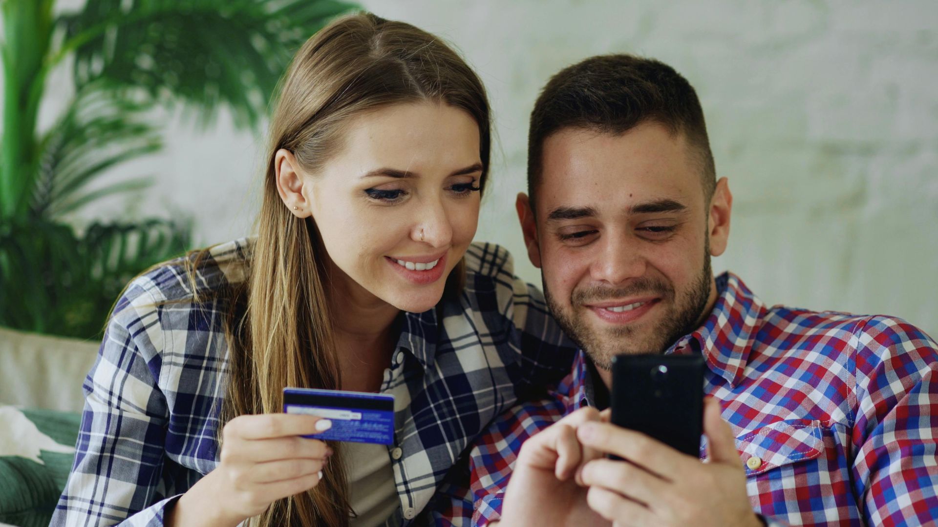 Happy couple shopping online using smartphone and credit card indoors.