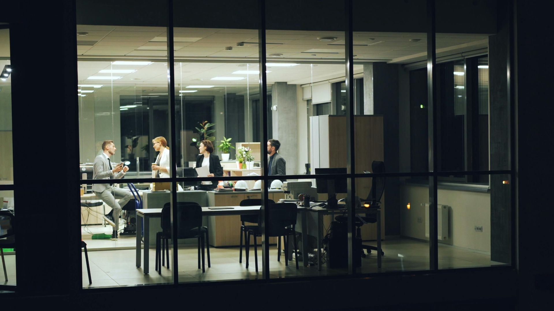 A nighttime office meeting with professionals working in a modern glass-walled office.