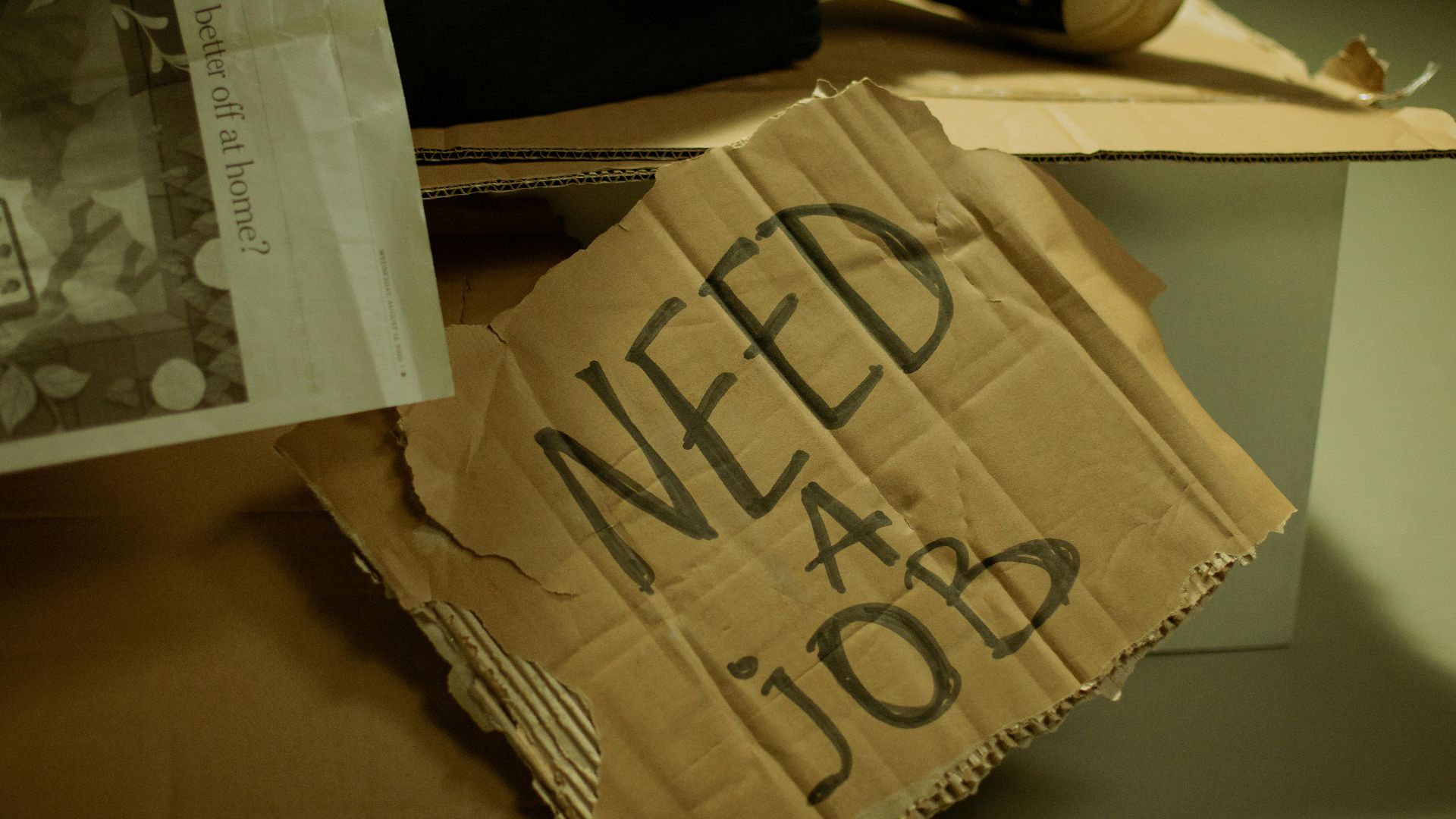 Close-up of a cardboard sign and newspaper depicting joblessness and unemployment.